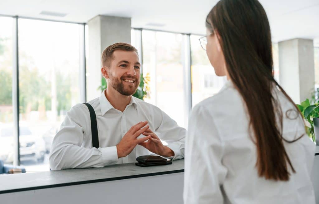 Friendly customer. Man in white shirt is ordering a room in the hotel by woman's help